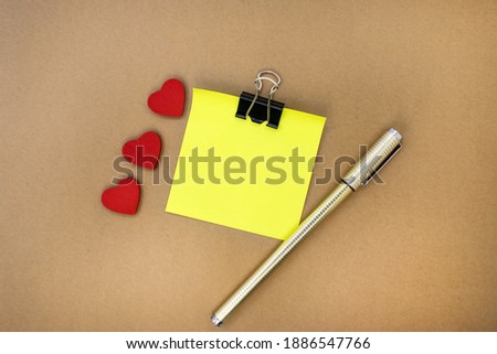 On a brown background is a yellow blank sheet with three red hearts and a yellow pen. Greeting card for greetings and wishes