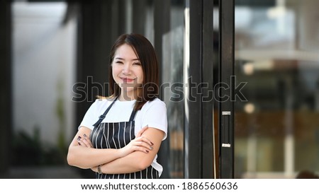 Startup successful small business owner woman standing with arms crossed and smiling to camera at her coffee shop.