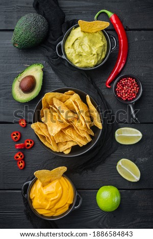 Triangular yellow corn tortilla chip with sauces, on black wooden background, top view or flat lay