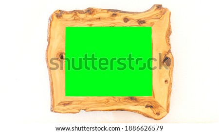 A picture frame made of wood, irregular borders, containing an empty green rectangle. Isolated on a white rough wall.
