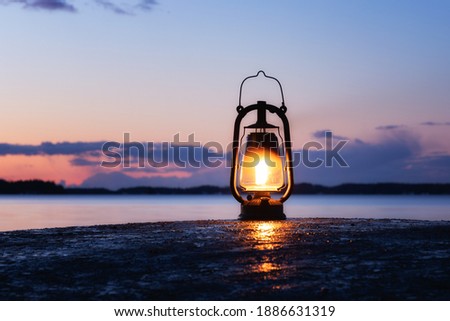 An old vintage oil lantern on a rock by the sea. Beautiful sunset sky and sea on background. Chill out travel concept. Royalty-Free Stock Photo #1886631319