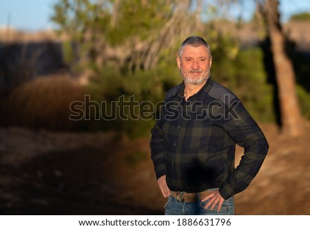 Portrait of an elderly man with a beard and gray hair. A photo with a very soft background in the evening at sunset in warm light. The senior is wearing jeans.