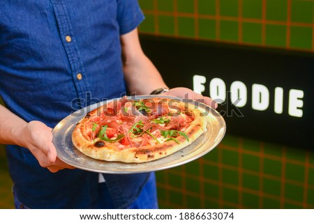Waiter carrying plate with a tasty italian pizza. Italian cuisine concept, word foodie written on the background. Fast food, junk food concept.