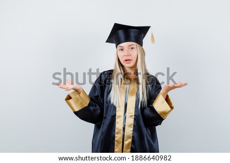  blonde girl stretching hands in questioning manner in graduation gown and cap and looking perplexed , front view. 