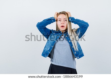  young lady in t-shirt, denim jacket, skirt holding hands on head and looking forgetful , front view. 