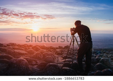 man photographer holding a camera to shoot nature sunrise at mountain scenery.Tourists take pictures of sunset nature with camera on a tripod with copyspace.