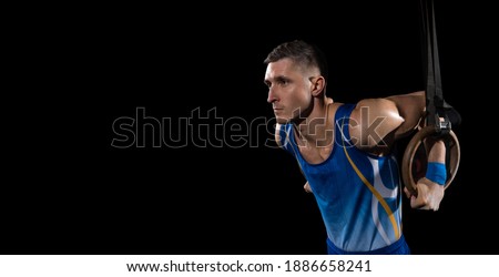 Flyer. Muscular male gymnast training in gym, flexible and active. Caucasian fit guy, athlete in blue sportswear doing exercises for strength, balance. Movement, action, motion, dynamic concept.