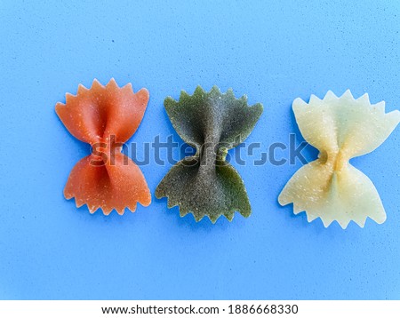 Colorful penne pasta isolated on blue background. Red, green and white pasta. Top view 