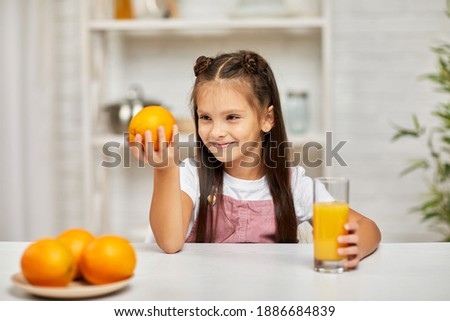 little child girl holding oranges and juice in the kitchen. choice between fruit and fresh juice