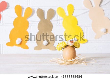 Easter egg in a basket. Easter egg decorated with yellow roses wreath and paper bunnies