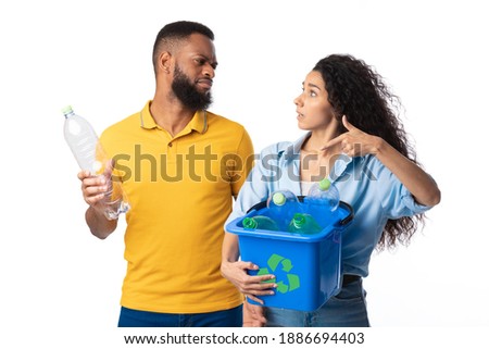 Husband Refusing To Sort Waste Having Quarrel With Wife While She Holding Box With Recycle Symbol And Plastic Litter Standing On White Studio Background. Junk Disposal, Recycling And Trash Sorting