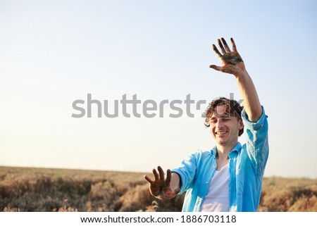 Portrait of male artist with stained with paint hands, having fun on wheat field in summer, smiling. Painting workshop in rural countryside. Artistic education concept. Outdoors leisure activities.