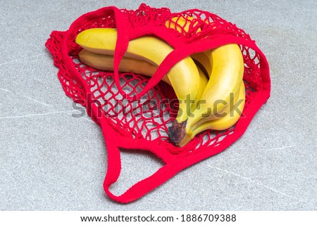 Shopping food concept. Yellow bananas lying in a red shopping bag on a gray Ultimate trending 2021 background, top view, close-up. Healthy food concept
