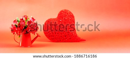 Red alstroemerias in a watering can with a red heart on St. Valentine's Day. Banner