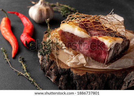 still life composition with a piece of red smoked dry ham on a wooden cross section of the tree, side view