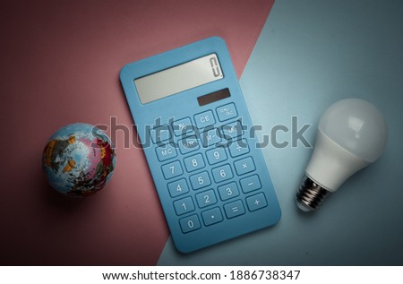 Energy saving. Calculator with led light bulb and globe on blue pink pastel background. Save planet. Eco concept. Top view