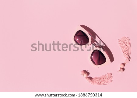 Composition made with woman accessories. Sunglasses and earrings on pink background. Creative monochrome layout. Fashion and summer concept. Flat lay. Top view. Copy space