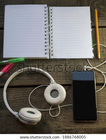cuadernocon lapiz y resaltadores, telefono para escuchar musicar e inspirarse, sobre mesa de madera