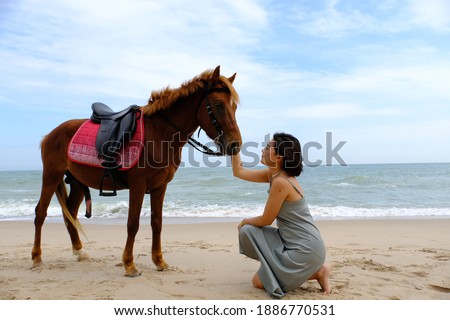 Beautiful asian woman sit on the sand beach and fondle the brown horse at Hua Hin beach, Prachuap Khiri Khan, Thailand