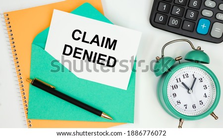 Card on a postal envelope with the text CLAIM DENIED, clock, calculator, pen.