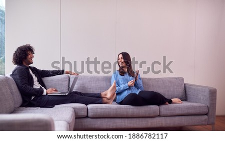 Relaxed Young Couple At Home Sitting On Sofa Using Digital Tablet And Laptop Computer