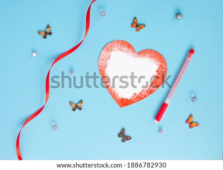 Romantic card on a blue background with a red heart made of paper, multicolored butterflies ribbons red pen lie around.