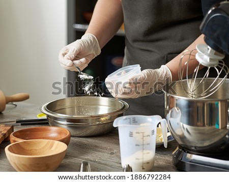 A closeup of a pastry chef adding flour or baking powder to a mixer bowl to make a dessert dough. Royalty-Free Stock Photo #1886792284