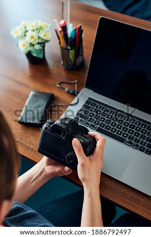 Female photographer working on photos on laptop and camera. Woman editing retouching browsing photos working as a freelancer sitting at desk