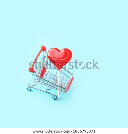 Shopping cart with red heart lollipop on abstract blue background. romantic sweet gift. symbol of love. Valentine's day, 14 february concept. top view. copy space. element for design.
