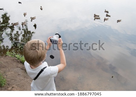 The child pointed the camera at the ducks. Ducks swim in the lake. Yun is a photographer.