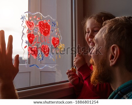 Child with father painting Love sign, playing indoors quarantine family leisure. Little girl holds paintbrush in hand draws red heart on window glass. Valentine's day. Stay home art concept New normal