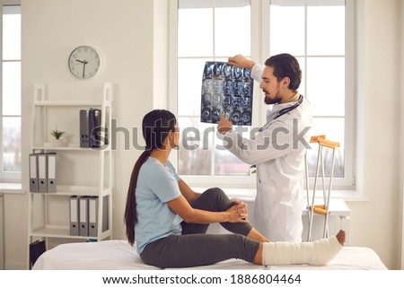 Woman listening to orthopedic doctor at hospital. Trauma surgeon or radiologist talking to patient, showing broken leg or foot fracture X-ray film, explaining treatment course, giving recovery advice