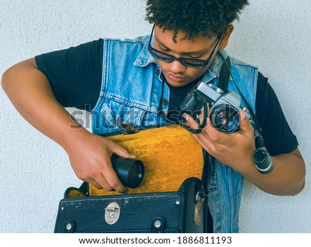 Curly haired boy in a denim jacket is taking out a lens to change it into his old analog camera.