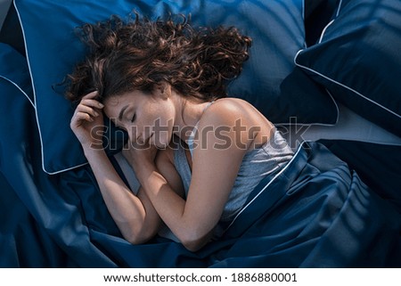 Top view of young woman sleeping on side in her bed at night. Beautiful girl sleeping profoundly and dreaming at home with blue blanket. High angle view of woman asleep with closed eyes. Royalty-Free Stock Photo #1886880001