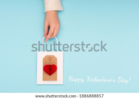Blue background with craft paper red heart in woman hand. Greeting card for Valentines, Woman or Mothers Day. Flat lay, top view, copy space.