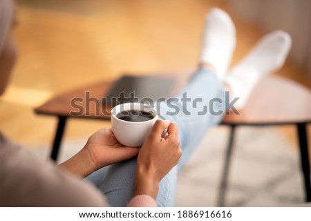 Closeup of young black woman warming her hands on cup of coffee, relaxing at home, empty space. Unrecognizable lady with aromatic hot beverage enjoying peaceful relaxing time on day off Royalty-Free Stock Photo #1886916616