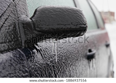 Ice-covered car side mirror with icicles, glass and side doors in perspective, icy vehicle on a winter day after freezing rain in Russia Royalty-Free Stock Photo #1886937556
