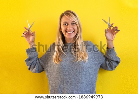 Young blond woman hold scissers. One Person cute smiles and delight. Colors of 2021 year, Girl wearing grey on yellow background. Hairdressers and beauty salons.  Haircut for girls
