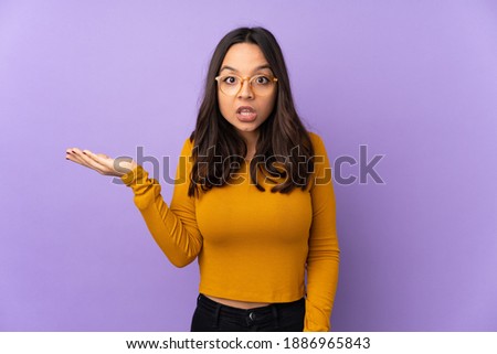 Young mixed race woman isolated on purple background making doubts gesture