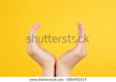 
hands of teenage girl forming a cup on isolated yellow studio background