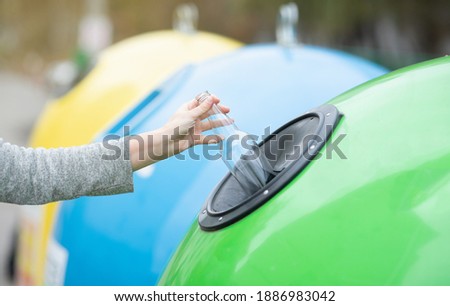 Waste Sorting And Recycling Concept. Unrecognizable female throwing empty glass bottle into green recycle bin garbage container outdoors, caring about environment, cropped image with selective focus Royalty-Free Stock Photo #1886983042