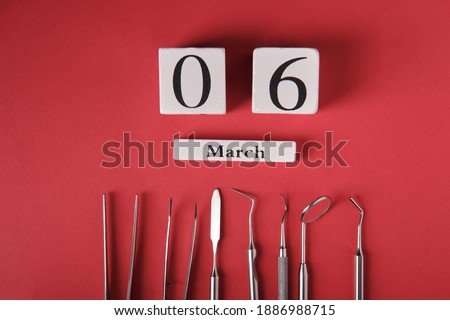 Wooden calendar with date 6 march, international day of the dentist, dental instruments, on a red background, top view