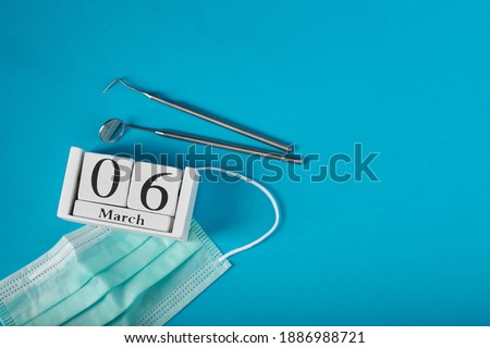 Wooden calendar with date 6 march, international day of the dentist, dental instruments, on blue background, top view