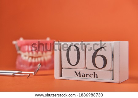 Wooden calendar with date 6 march, international day of the dentist, dental instruments, on orange background, side view