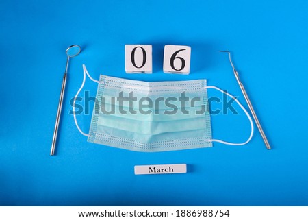 Wooden calendar with date 6 march, international day of the dentist, dental instruments, on blue background