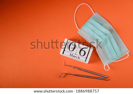 Wooden calendar with date 6 march, international day of the dentist, dental instruments, on orange background