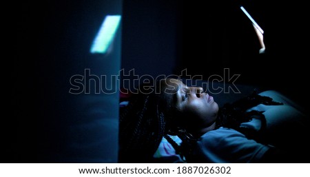 Black girl looking at cellphone screen at night lying in bed with bright blue light