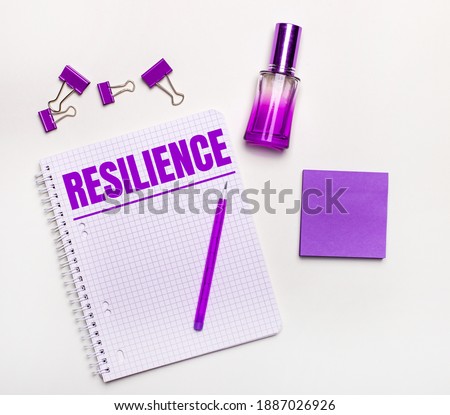 On a light background - a lilac gift, perfume, lilac business accessories and a notebook with a lilac inscription RESILIENCE. Flat lay. Womens business concept