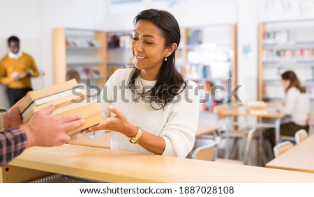 Portrait of young adult woman returning books to librarian at public library Royalty-Free Stock Photo #1887028108
