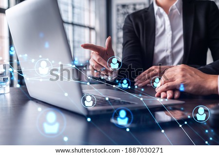 Two HR specialists analyzing the recruitment market using laptop to boost the intern program at international consulting company. Social networking hologram icons. Royalty-Free Stock Photo #1887030271